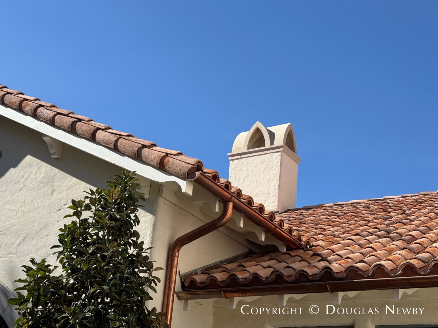 A roof detail at 4400 Belfort Place in Highland Park, Dallas, Texas, that shows the red barrel tile roof, stone decorative chimney cap, copper gutters, bracketed soffits and hand-troweled plaster.